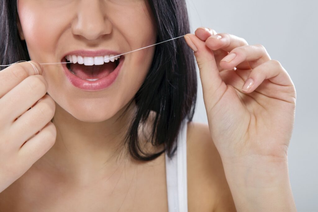 Close-up of a woman flossing her teeth to maintain oral hygiene and prevent plaque buildup.